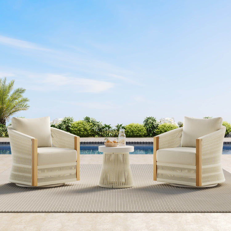Two woven outdoor chairs with cushions and a small table by a pool, under a clear sky.