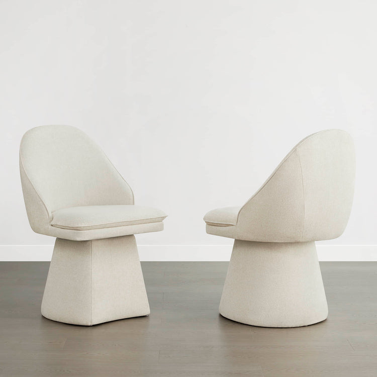 Alt: Two cream-colored swivel chairs with a modern design, placed on a wooden floor against a plain white wall.