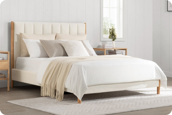 A cozy bed with a white upholstered headboard, light wood frame