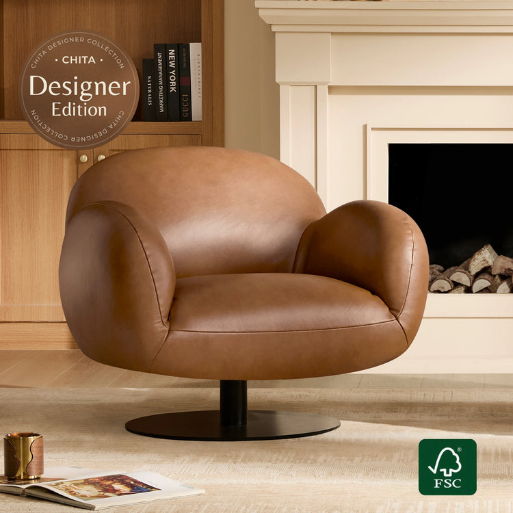 A brown leather swivel armchair with a black round pedestal base, shown in a styled living room setting with a fireplace and bookshelf in the background. A circular badge reads 'CHITA Designer Edition' and an FSC logo is visible in the corner.