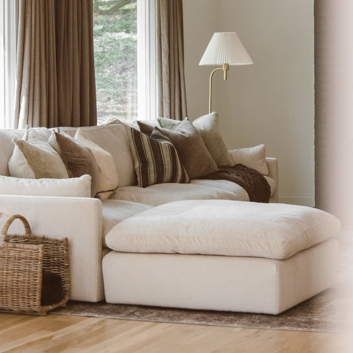 A cozy beige sofa with plush pillows, a throw blanket, and a wicker basket next to a floor lamp.