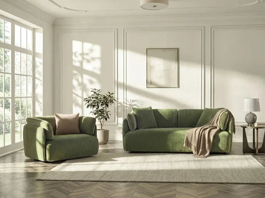 Green armchair and sofa on a rug in a sunlit living room with a large window.