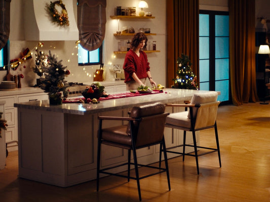 A woman in a red sweater preparing food in a cozy, festively decorated kitchen with Christmas trees and lights.