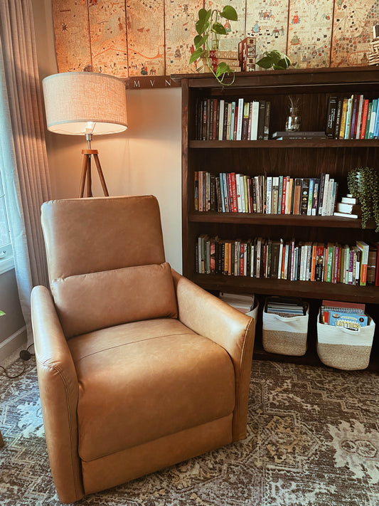 A cozy reading nook with a brown leather chair, a wooden bookshelf filled with books, and a patterned rug.