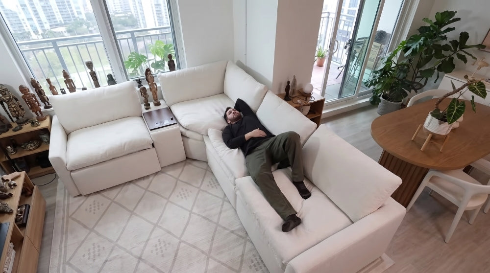 A man relaxing in the zero gravity position on a white modular reclining sofa, demonstrating ergonomic support and personalized comfort in a spacious, plant-filled modern living room setup.