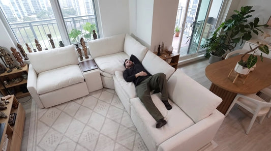 A man relaxing in the zero gravity position on a white modular reclining sofa, demonstrating ergonomic support and personalized comfort in a spacious, plant-filled modern living room setup.