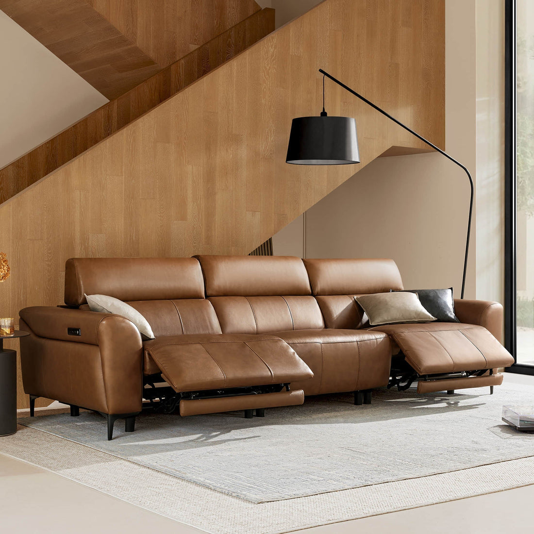 Brown leather reclining sofa with chaise and black floor lamp in a wood-paneled modern living room.