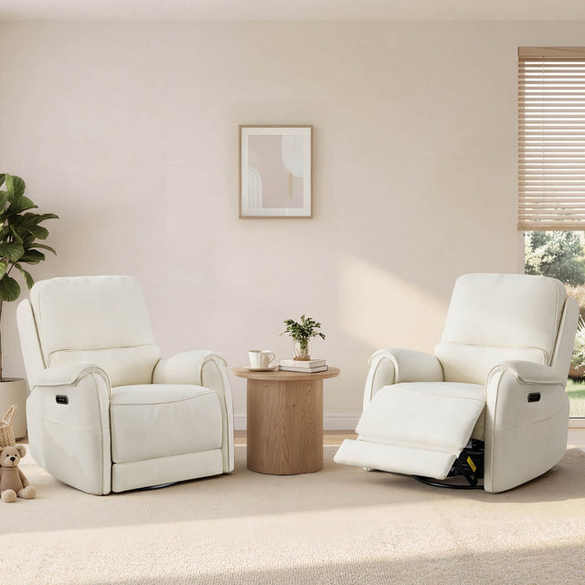 Two ivory power recliners sit beside a round wood table in a sunlit living room with plants, blinds, and soft neutral decor.