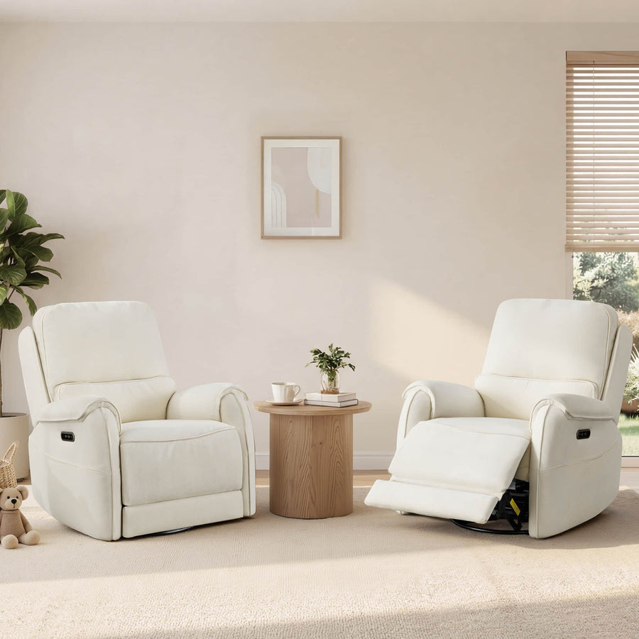 Two ivory power recliners sit beside a round wood table in a sunlit living room with plants, blinds, and soft neutral decor.