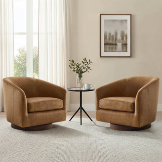 Two caramel brown barrel lounge chairs sit beside a small black table in a bright neutral room with soft curtains.
