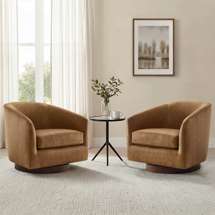 Two caramel brown barrel lounge chairs sit beside a small black table in a bright neutral room with soft curtains.