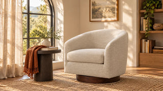 Beige barrel swivel chair with a wood base beside a small table and arched window.