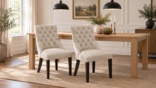 Two beige button-tufted dining chairs paired with a simple wood table and black pendant lights.