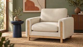Cream wide-seat armchair with an exposed light wood base against a sage wall.