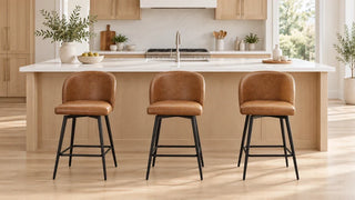 Three cognac upholstered stools evenly spaced beside a long white kitchen island.
