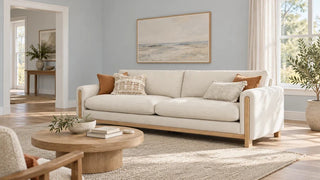 Ivory sofa with an exposed wood base in a pale blue-gray living room with an open doorway.