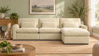 A cream Ivy sectional with an arm throw beside a scratching post and tabby cat
