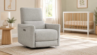 Gray Tracee nursery glider recliner beside a wood side table, with an empty crib in the background.