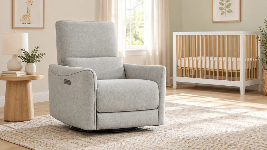 Gray Tracee nursery glider recliner beside a wood side table, with an empty crib in the background.