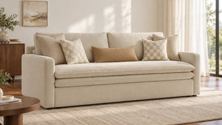 A cream sofa styled with two pairs of square pillows and one camel lumbar pillow.