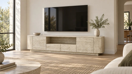 A wide travertine-look TV console beneath a wall-mounted television in a bright living room.