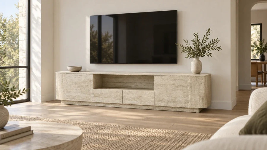 A wide travertine-look TV console beneath a wall-mounted television in a bright living room.