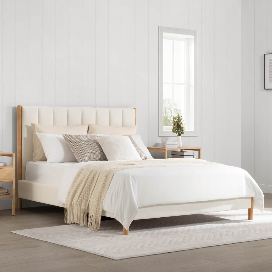 A complete upholstered bed anchors a bright bedroom, showing the overall relationship between mattress height and visible headboard area.
