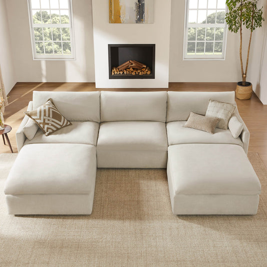 Cream performance fabric modular sectional sofa with two chaise lounges in a sunlit living room with wood floors, fireplace, large windows, neutral pillows, and a potted tree.
