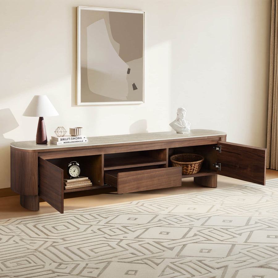 Modern wooden TV stand with open drawers and doors, topped with decor and books.