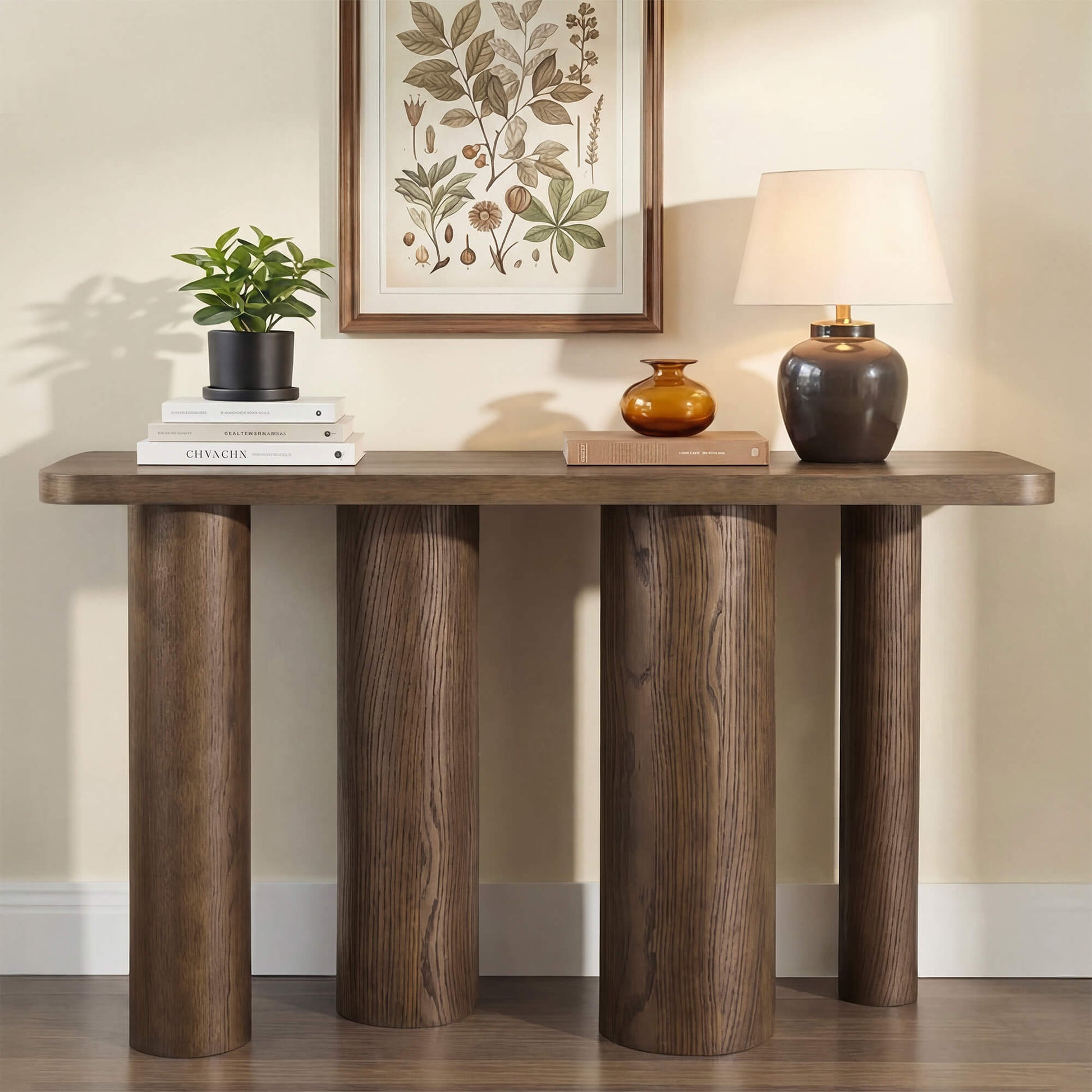 55" Eason mid-century oak wood console table with thick sculptural legs, topped with a plant, books, and a lamp.