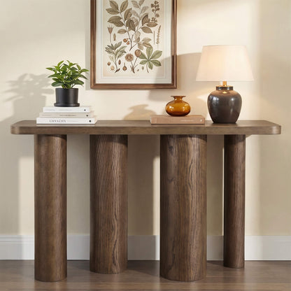 55" Eason mid-century oak wood console table with thick sculptural legs, topped with a plant, books, and a lamp.