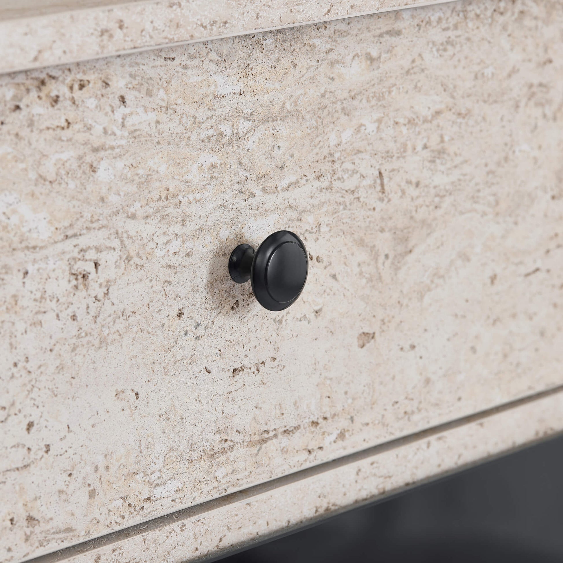 Close-up of a black round knob on a beige travertine fireplace sideboard.