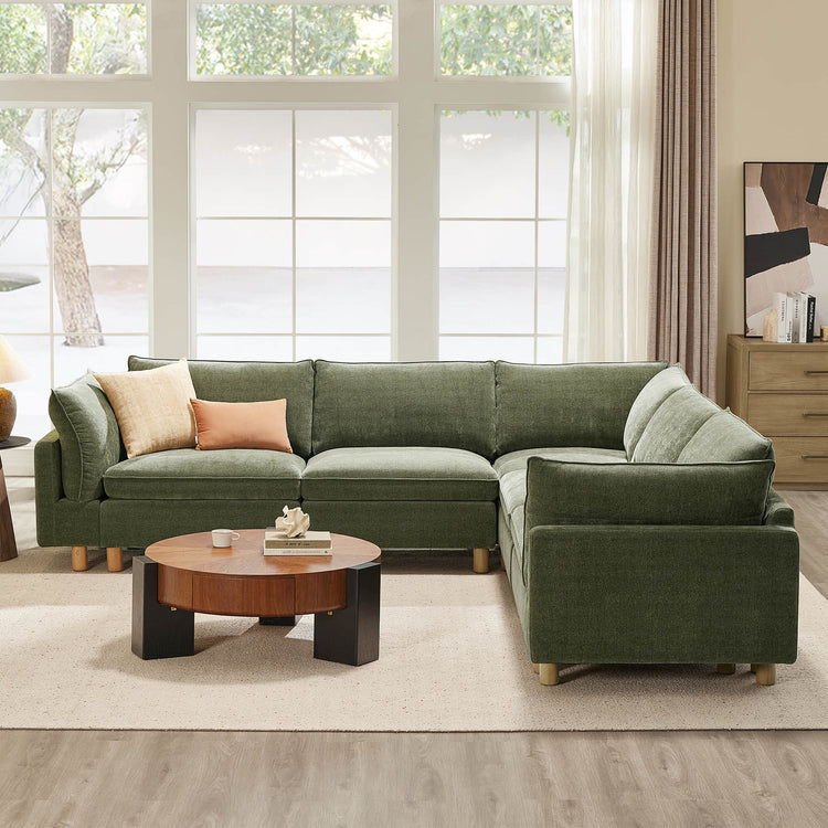 Green modular corner sectional sofa with wood legs and plush cushions, featuring two accent pillows on a beige rug.