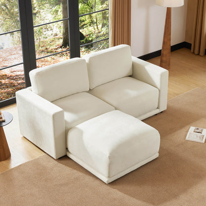 Beige sectional sofa with an ottoman in a bright living room with large windows, a floor lamp, and a neutral-toned rug. The room is filled with natural light and has a cozy, inviting atmosphere.

