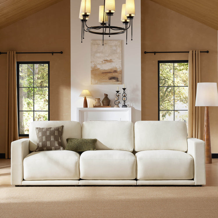  Front view of a beige modular sectional sofa in a cozy living room with decorative pillows, a chandelier, and large windows.