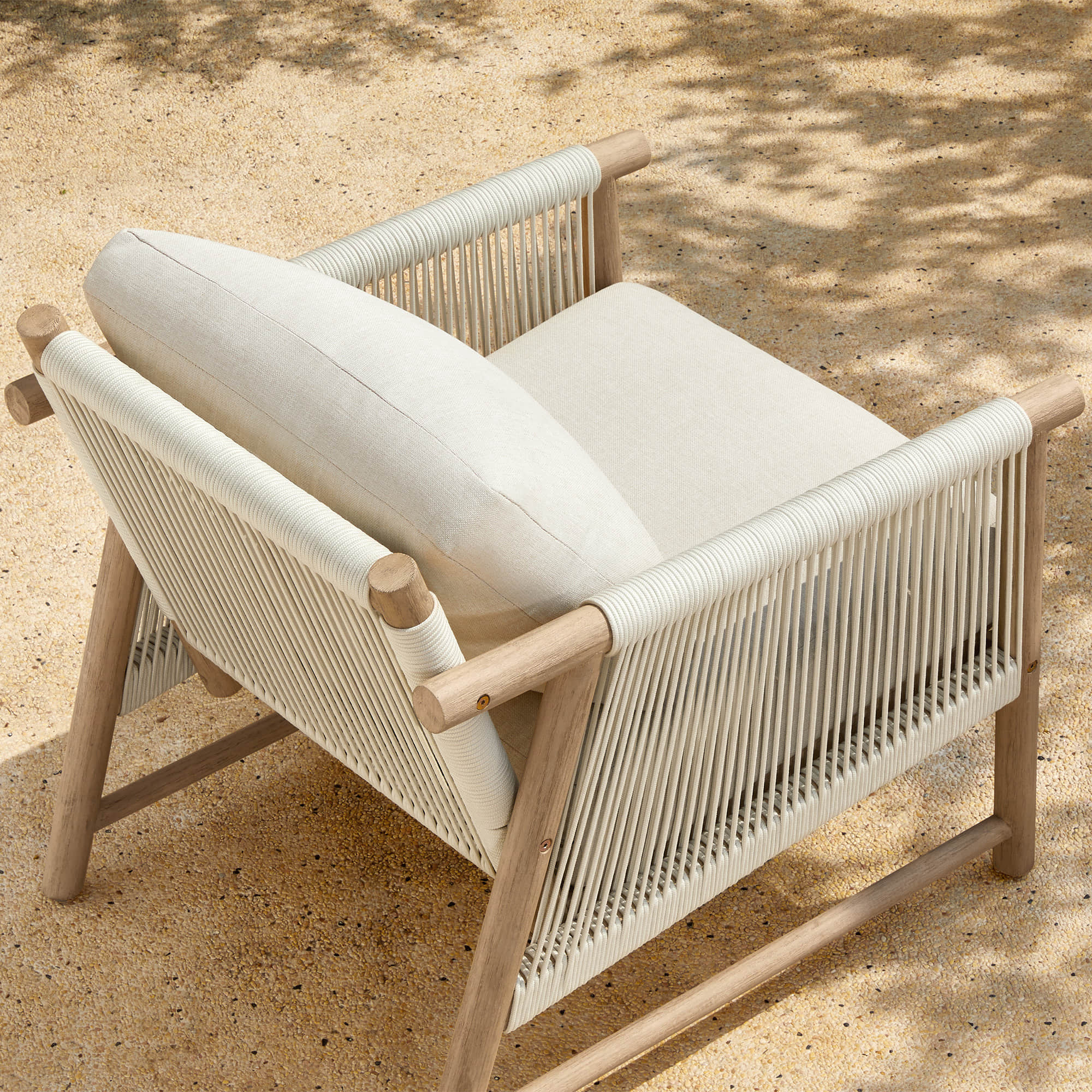 A Sienna Modern Acacia wood woven outdoor lounge chair with a cushion, set on a sandy surface.
