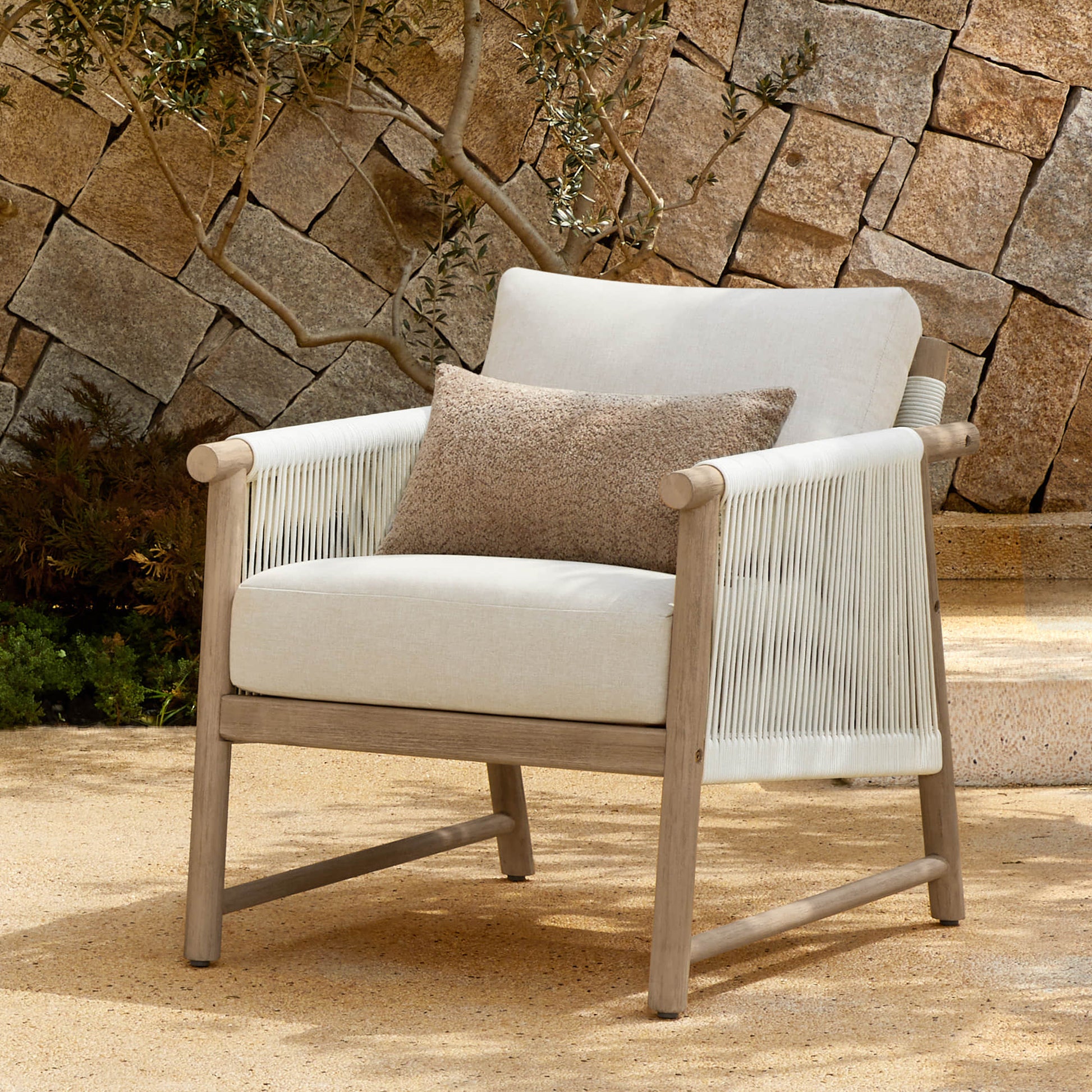 A Sienna Modern Acacia Wood Woven Outdoor Bistro Set chair with light beige cushions and a brown pillow