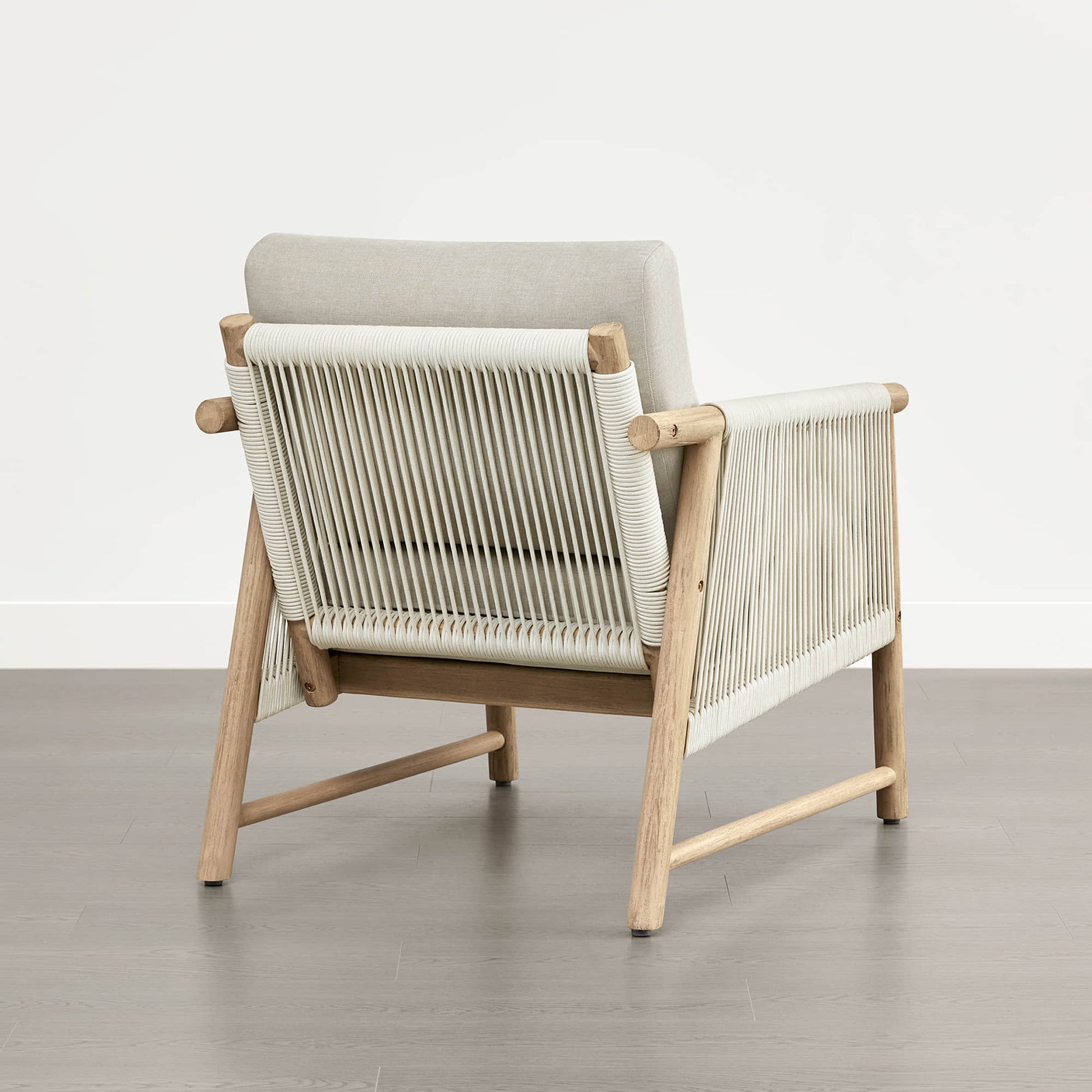 A Sienna Modern Acacia Wood Woven Outdoor Bistro Set chair with light beige cushions and woven back, on a wooden floor.