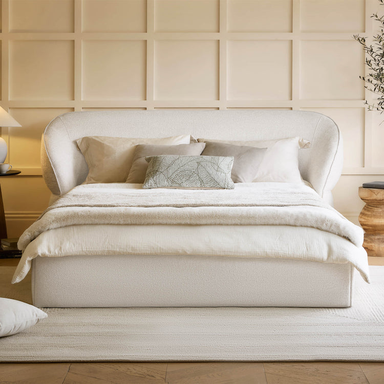 Beige upholstered bed with pillows against a paneled wall.