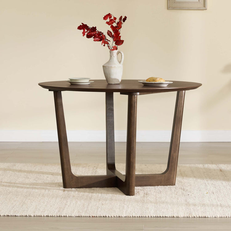 Rory Round Wood Cross-Base Dining Table in walnut finish with a vase of red flowers and plates on top.