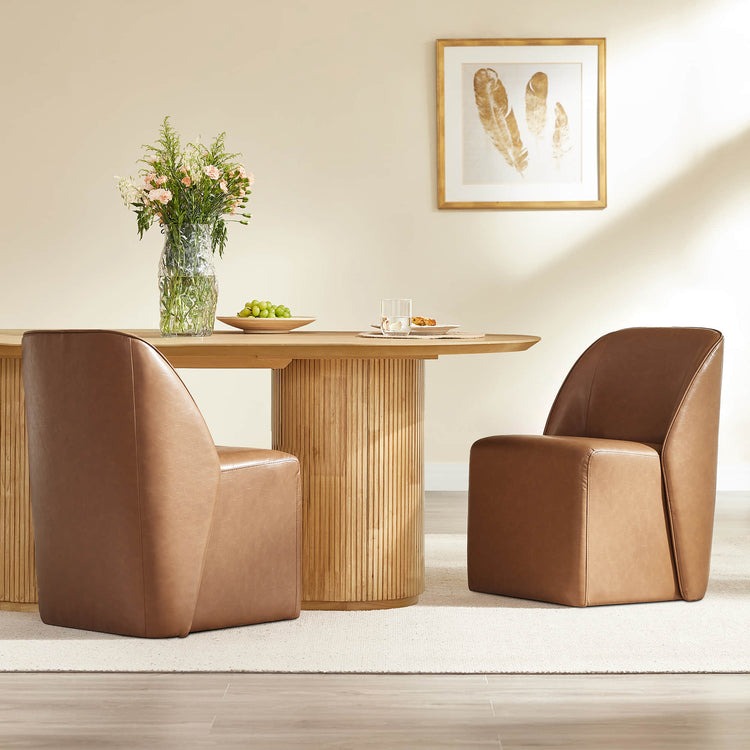 Two Soren leather rolling dining chairs in saddle brown with caster bases sit beside a fluted wood pedestal dining table.