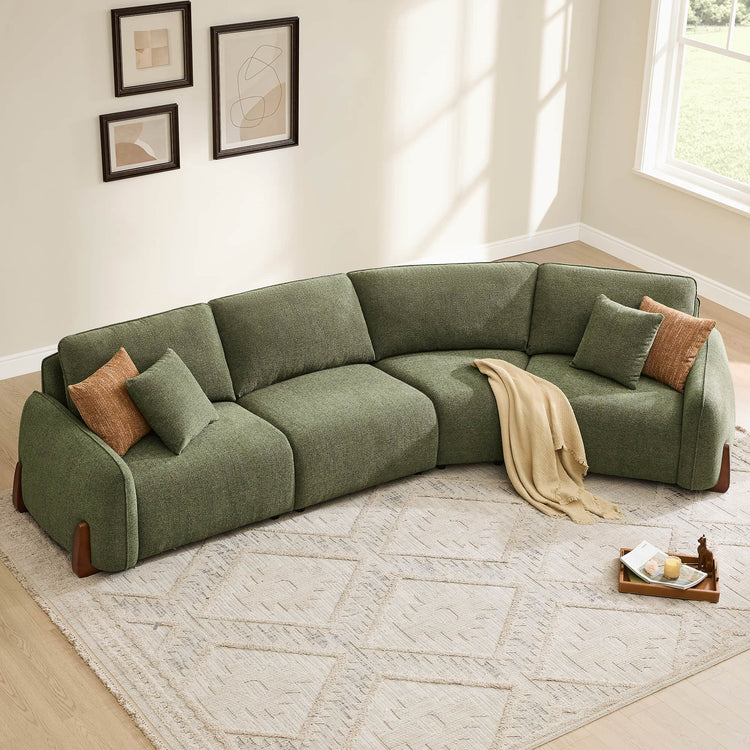 Green modular curved sofa with wood legs and textured fabric, featuring two accent pillows and a beige throw blanket.
