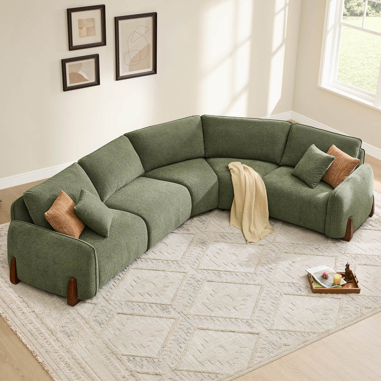 Moss green Teleri 5-seat modular curved sofa with wood legs, styled in a modern living room on a geometric rug.