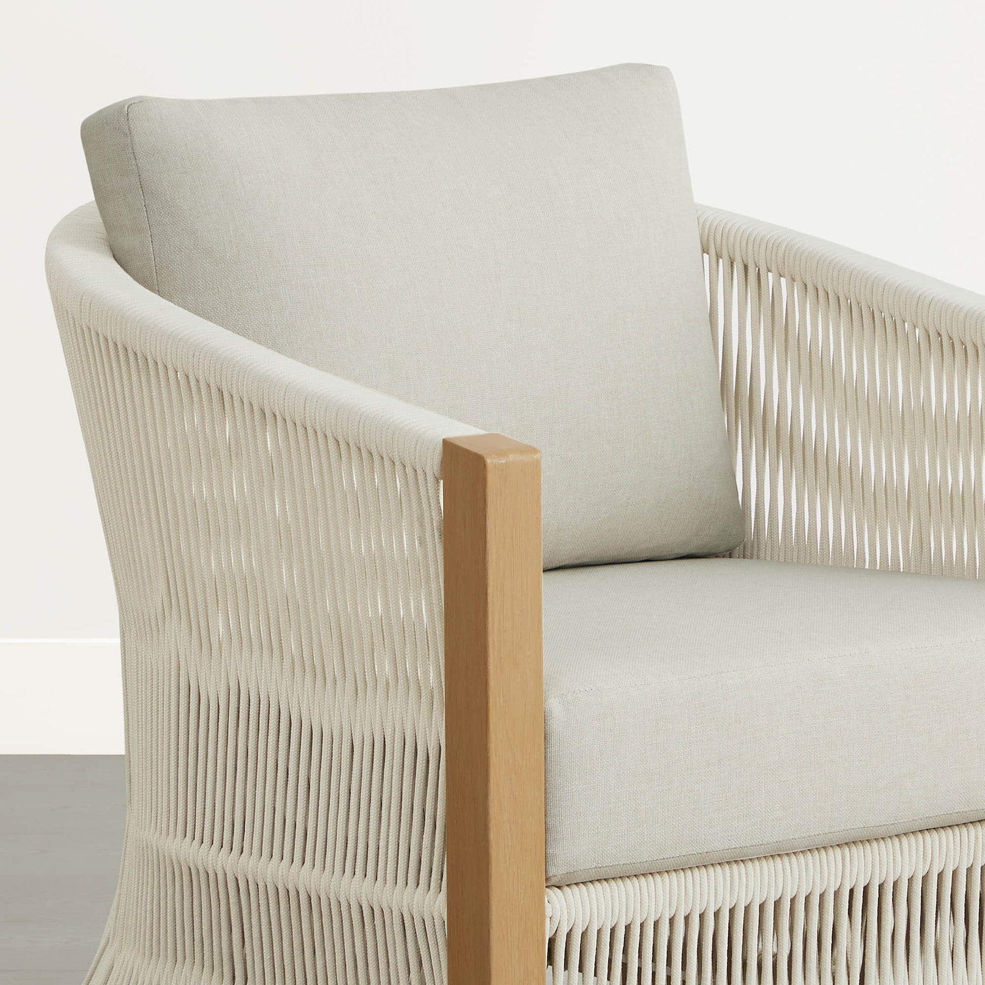 A close-up of a woven outdoor lounge chair with light wood accents and cream cushions.