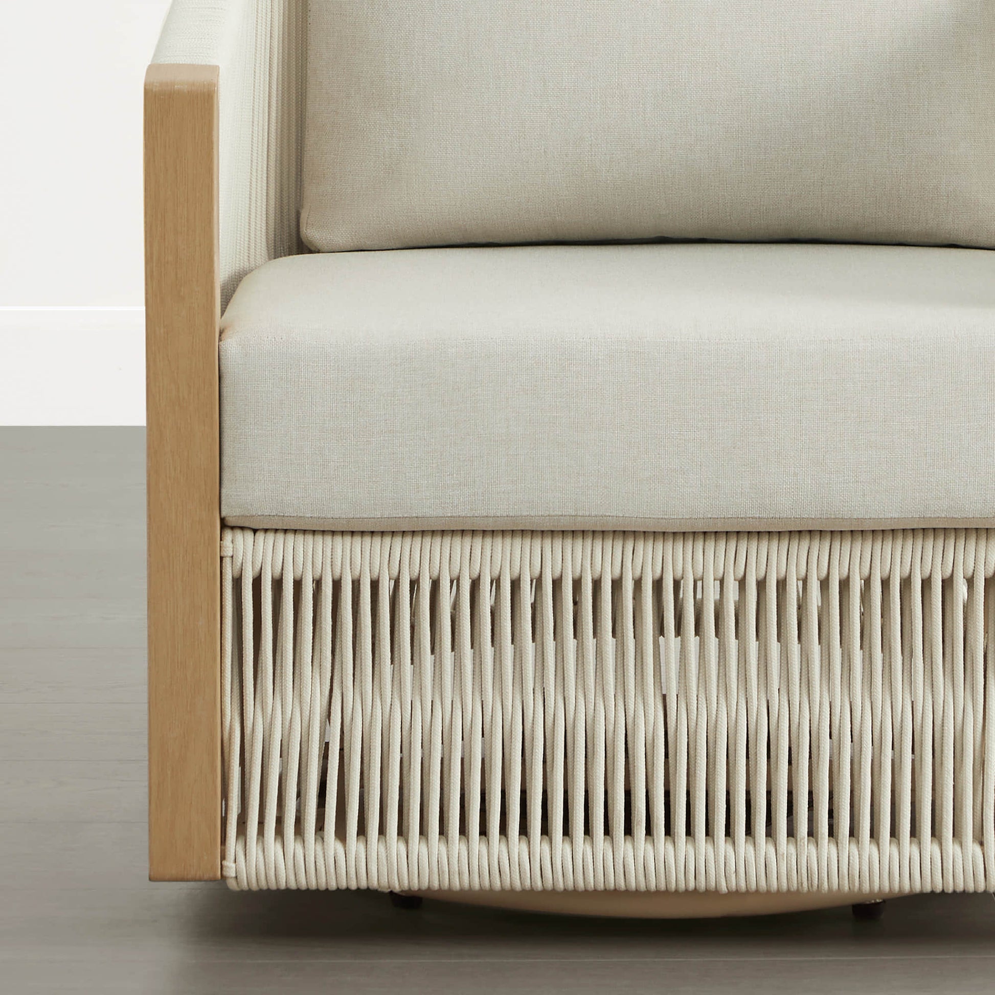 A woven outdoor lounge chair with cream cushions and a light wood frame, viewed from the side.