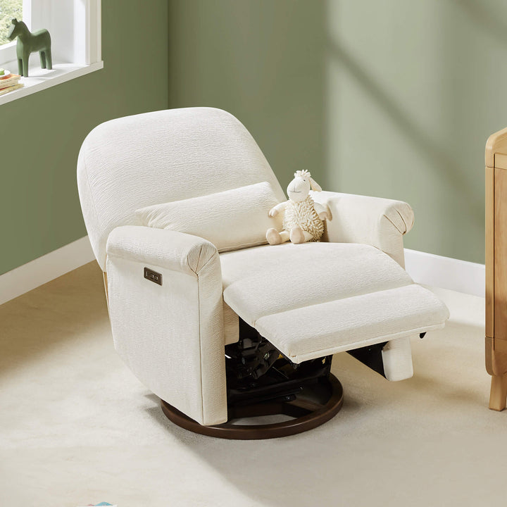 Aurora Power Swivel Nursery Glider Recliner, beige, in a nursery with a stuffed sheep and natural light.