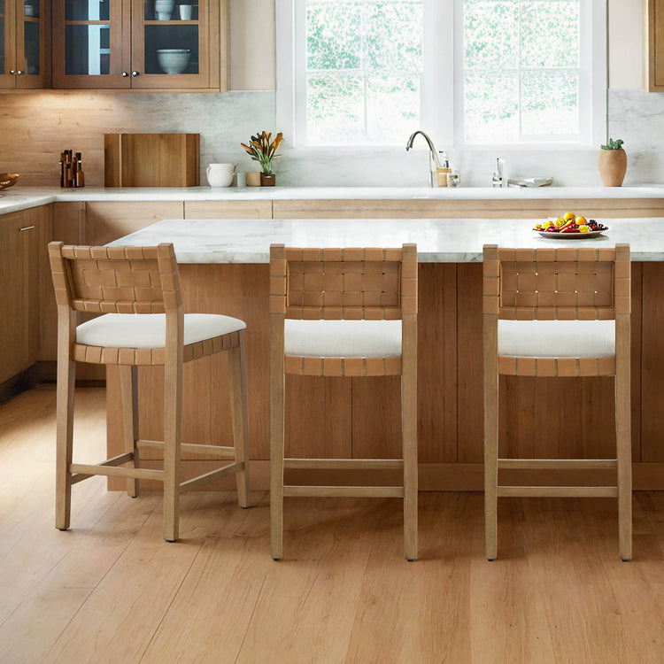 Aries Mid-century Modern Handwoven Counter Stools with woven leather backs and white cushions, placed around a kitchen island.