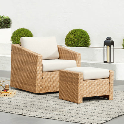 A wicker chair with a matching ottoman, both cushioned, on a patio near a lantern and plants.