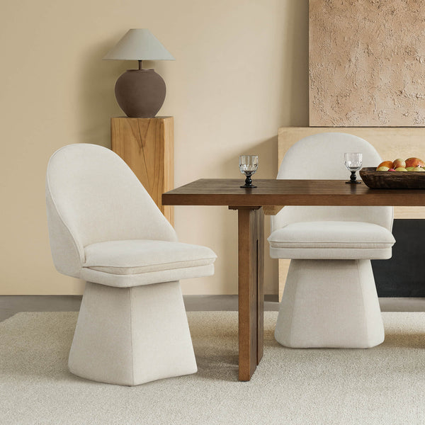 Two beige swivel chairs positioned by a wooden dining table, with a decorative lamp and light-colored wall in the background.