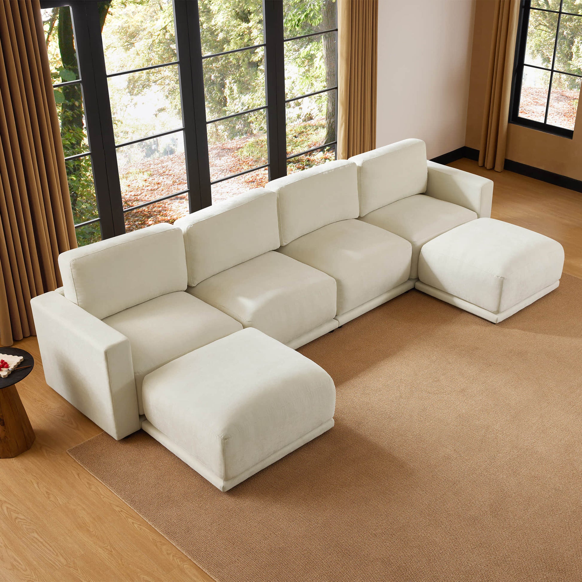 Aerial view of a modern sectional sofa with a minimalist design, set in a cozy room with large windows and a natural color palette.